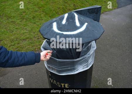 gros plan de la main de l'enfant mettant ses déchets dans un bac à litière avec un visage souriant dehors sur la chaussée en hiver Banque D'Images