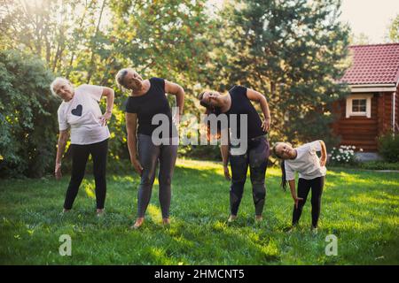 Famille semblable avec des femelles de quatre générations réchauffant les corps étirants pour garder la forme debout sur la prairie pleine d'herbe verte et d'arbres. Passer du temps Banque D'Images