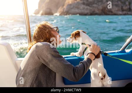 Vue arrière jeune adulte femme caucasienne profiter de petting mignon adorable petit Jack russel chien voile famille bateau de luxe contre bleu eau brillant Banque D'Images