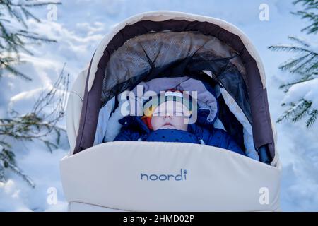 Bébé garçon dormant dans un pram Noordi, parc d'hiver près des arbres enneigés. Enfant en bas âge dans une poussette Noordi - Moscou, Russie, 04 février 2022 Banque D'Images