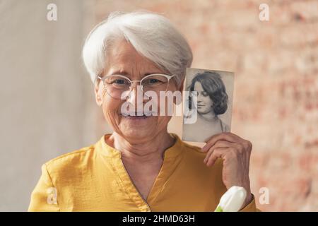 sourire et contenu grand-mère aux cheveux gris se comparant à son vieux portrait noir et blanc . Photo de haute qualité Banque D'Images