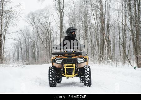 Homme sur un quad en hiver. Portrait d'un rider quadricycle dans une forêt enneigée Banque D'Images