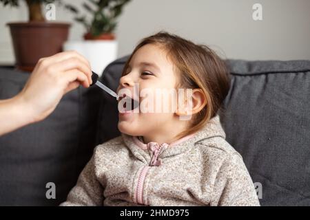 Portrait d'une jeune fille d'âge préscolaire de race blanche prenant des vitamines avec des gouttes à la maison. Concept d'immunité Banque D'Images