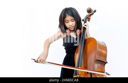 Un enfant asiatique aime la musique classique avec un instrument à cordes de violoncelle sur fond blanc isolé. Concept de classe d'éducation musicale Banque D'Images