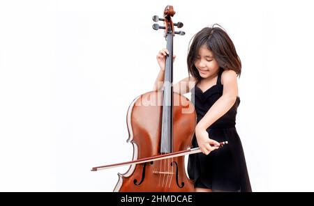 Un enfant asiatique aime la musique classique avec un instrument à cordes de violoncelle sur fond blanc isolé. Concept de classe d'éducation musicale Banque D'Images