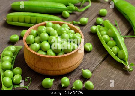 Petits pois verts frais dans un bol en bois, gousses de petits pois verts sur une table en bois. Nourriture végétalienne Banque D'Images