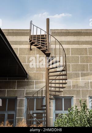 L'escalier en colimaçon en métal brun avec rambarde en fer mène du balcon sur le toit au premier étage devant un mur texturé en briques. Mise au point sélective. Banque D'Images