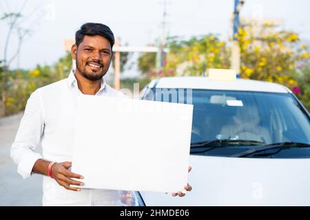 Le chauffeur de cabine souriant est heureux avec un tableau blanc vide ou un écriteau devant la voiture en regardant la caméra - concept de service de transport, lui-même Banque D'Images