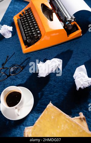 vue de dessus d'une tasse à café près d'une machine à écrire vintage, de lunettes et de papier froissé sur une nappe en velours bleu Banque D'Images