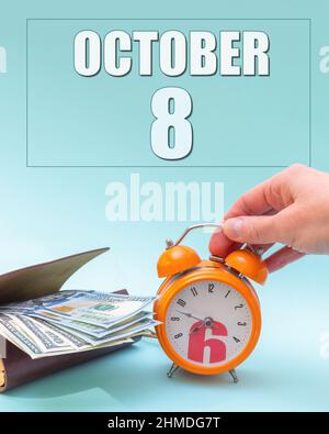 Octobre 8th. Main tenant un réveil orange, un portefeuille avec de l'argent et une date calendrier. Jour 8 du mois. Planification des activités. Le temps, c'est de l'argent. Heure de taxe. A Banque D'Images