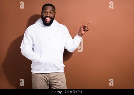 Photo de choqué charmant gars habillé blanc sweat-shirt pointant doigt vide espace isolé couleur marron fond Banque D'Images