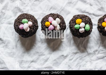 Petits gâteaux au chocolat de Pâques faits maison avec glaçage à la crème au beurre de chocolat et œufs de bonbons. Brunch de Pâques. Décoration printanière en fleurs. Table en lin blanc Banque D'Images