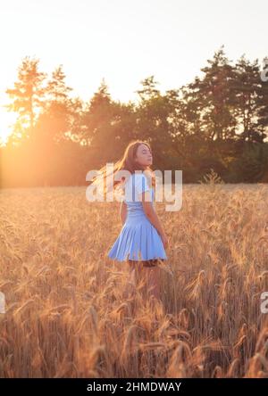 Une jeune fille heureuse est souriante au champ de blé, touchant des oreilles de blé avec sa main. Beau adolescent appréciant la nature au soleil chaud dans un champ de blé Banque D'Images