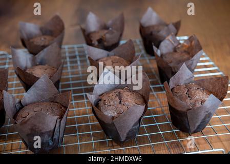 Muffins au chocolat dans une tasse de papier brun de cuisson par le dessus. Gros plan de petits gâteaux bruns avec des gouttes de chocolat. Banque D'Images
