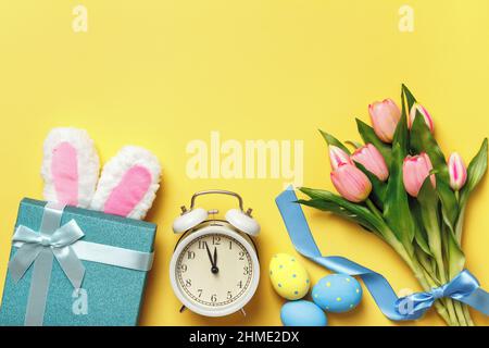 Œufs de Pâques réveil bouquet de tulipes cadeau rose avec oreilles de lapin sur fond jaune. Vue de dessus de l'espace de copie de la mise à plat. Banque D'Images