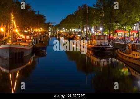 Pays-Bas. Canal nocturne d'Amsterdam et ciel sans nuages. Les péniches et les bateaux à moteur résidentiels sont amarrés avec réflexion dans l'eau Banque D'Images