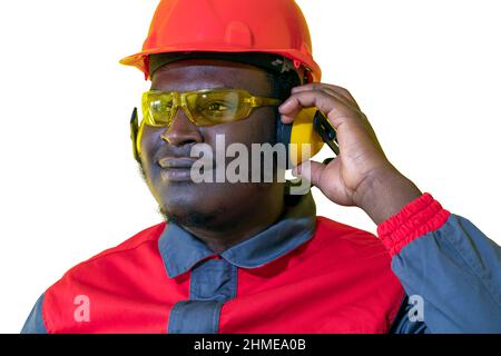 Jeune travailleur afro-américain en casque rouge, équipement de protection auditive et uniforme de travail. Banque D'Images