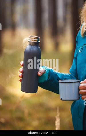 Thermos avec boisson chaude. Rafraîchissements pendant la randonnée. Femme tenant une tasse de voyage et un contenant à boisson isotherme Banque D'Images