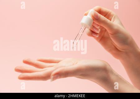 Une femme goutte le sérum d'une pipette dans la paume de sa main. Gros plan des mains sur fond rose. Copier l'espace. Le concept des produits de soins de beauté. Banque D'Images