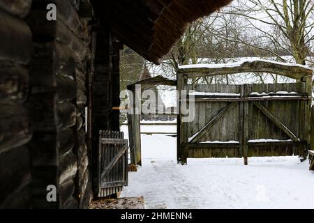 Une maison en rondins avec un toit de chaume. Cour avec clôture en bois et ancienne porte. Banque D'Images