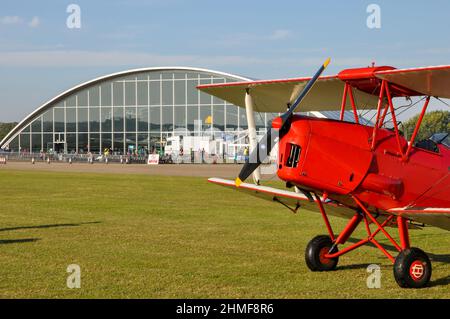 Tiger Moth biplan assis sur l'herbe à l'aérodrome de Duxford par le hangar de l'American Air Museum de Havilland DH82 Tiger Moth. Avion d'époque Banque D'Images