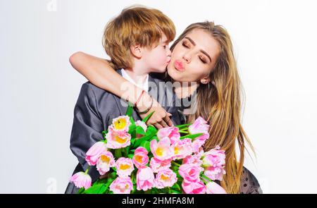 Mignon fils félicitant la mère avec un bouquet de tulipes le jour de la femme. Garçon embrasse la mère sur la joue. Banque D'Images