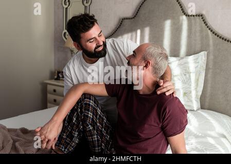 Heureux couple gay dans l'amour embrassant et tenant les mains dans le lit à la maison. Banque D'Images