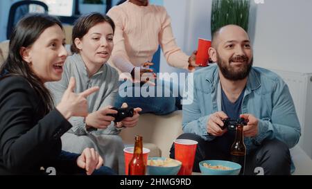 Gros plan de l'homme et de la femme utilisant des contrôleurs pour jouer à des jeux vidéo sur la console tv pour faire une activité amusante après le travail. Collègues qui s'amusant à jouer à la télévision et à boire au bureau après les heures d'ouverture. Banque D'Images