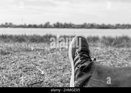 Jeune homme jambes chaussé dans des chaussures de running. Reposez-vous sur le chemin touristique sur la rive de la rivière Banque D'Images