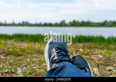 Jeune homme jambes chaussé dans des chaussures de running. Reposez-vous sur le chemin touristique sur la rive de la rivière Banque D'Images