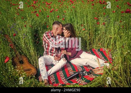 les amateurs de guitare boivent du vin dans le champ de fleurs. musique. couple amoureux. homme et femme dans le champ de pavot. Banque D'Images