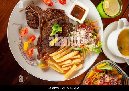 Steak d'os en T grillé moyen et rare avec salade, frites, tomates, purée de pommes de terre et épinards cuits au fromage sur une assiette blanche. Vue du dessus. Banque D'Images