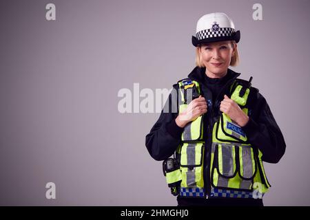 Studio Portrait d'une femme d'âge mûr, membre de la police, portant un chapeau contre un fond Uni Banque D'Images