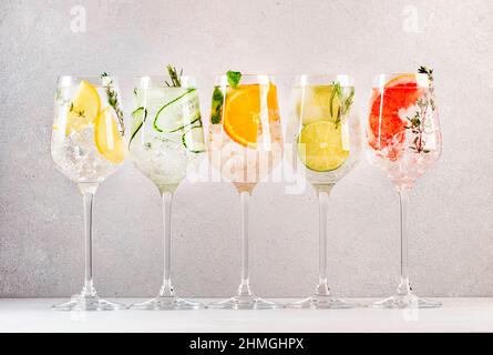 Ensemble de cocktails gin et tonique.Boissons alcoolisées à la mode avec citron vert, citron, pamplemousse, orange, concombre,soda et herbes épicées dans des verres à vin, dos gris Banque D'Images