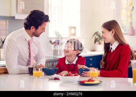 Père portant un costume ayant le petit déjeuner avec des enfants dans l'uniforme scolaire avant le travail Banque D'Images