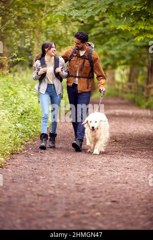 Couple avec chien Golden Retriever randonnée le long du chemin à travers les arbres dans la campagne Banque D'Images