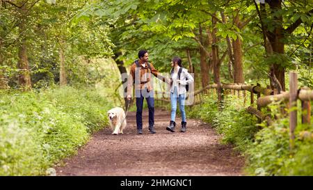 Couple avec chien Golden Retriever randonnée le long du chemin à travers les arbres dans la campagne Banque D'Images