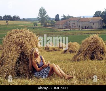 Jeune femme blonde à l'extérieur, assise par une cheminée de blé. Banque D'Images