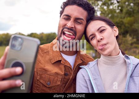 Couple à pied dans la campagne tirant des visages drôles comme ils prennent Selfie sur téléphone mobile Banque D'Images