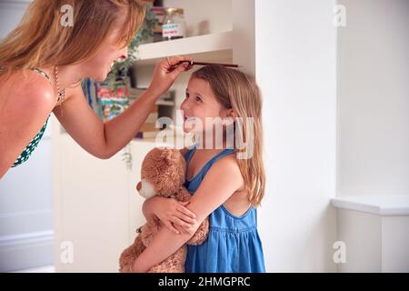 Mère mesurant la taille de la fille et marquant sur le mur à la maison Banque D'Images