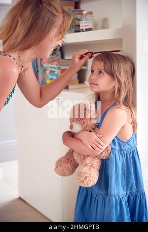 Mère mesurant la taille de la fille et marquant sur le mur à la maison Banque D'Images