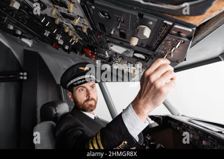 pilote dans le cap et uniforme atteignant le panneau supérieur dans le simulateur d'avion Banque D'Images