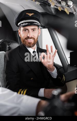 pilote barbu en uniforme montrant un copilote correct et souriant près d'un copilote flou Banque D'Images