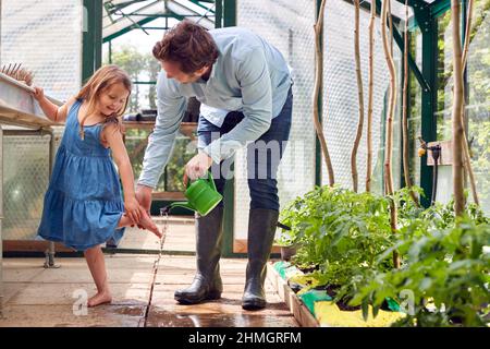 Le père lave les pieds de sa fille en utilisant un arrosoir car elle l'aide dans Greenhouse at Home Banque D'Images