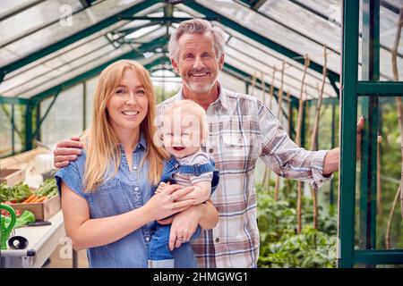 Portrait du grand-père avec la fille adulte et le petit-fils bébé debout à la porte de Greenhouse Banque D'Images