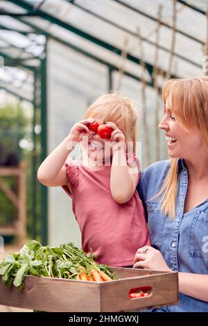 Mère avec fille en train de faire un visage drôle avec des tomates à la maison en serre Banque D'Images