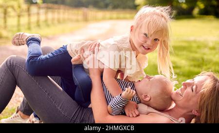 La mère et les enfants s'amusent à l'extérieur avec des enfants qui traînent au-dessus d'elle sur l'herbe Banque D'Images