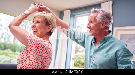 Couple romantique senior retraité dansant dans le salon à la maison ensemble Banque D'Images