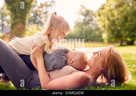La mère et les enfants s'amusent à l'extérieur avec des enfants qui traînent au-dessus d'elle sur l'herbe Banque D'Images