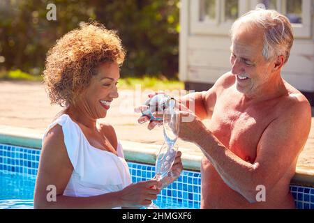 Un couple senior à la retraite se détendant dans la piscine pendant les vacances d'été célébrant l'ouverture du champagne Banque D'Images